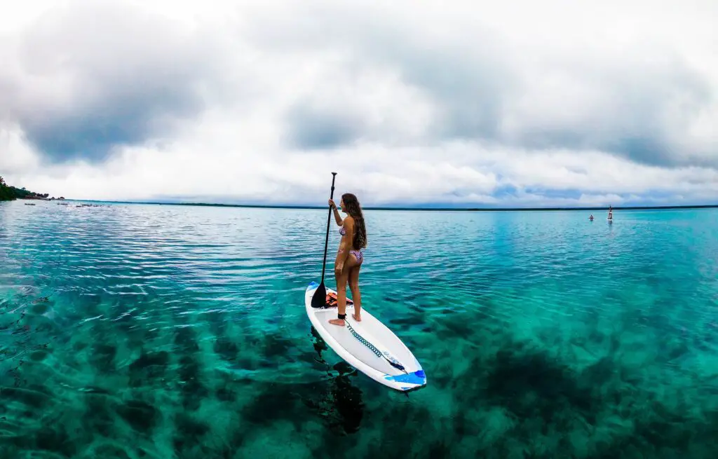 Una mujer parada en una tabla de remo disfruta de las aguas abiertas y las hermosas vistas a su alrededor.